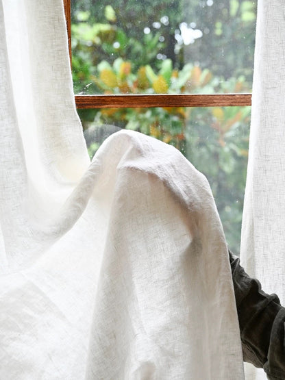 sheer white linen curtain draping by window with blurred outdoor greenery background