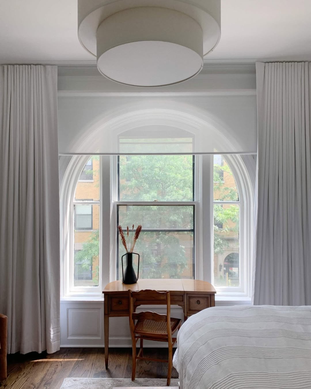 Solar shades installed in a modern bedroom, filtering sunlight through arched windows.