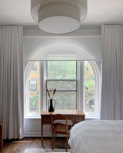 Solar shades installed in a modern bedroom, filtering sunlight through arched windows.