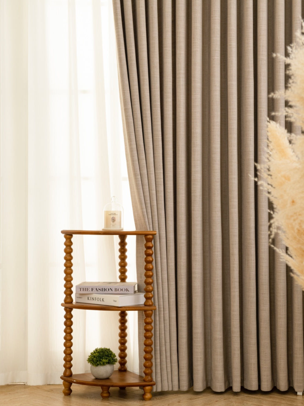 Contemporary living room decor with gray pleated linen blend drapes and white sheer curtains, wooden side table displaying home decor book and plant