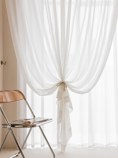 Elegant white sheer curtains with ribbon tie-back, enhancing natural light in a modern home setting
