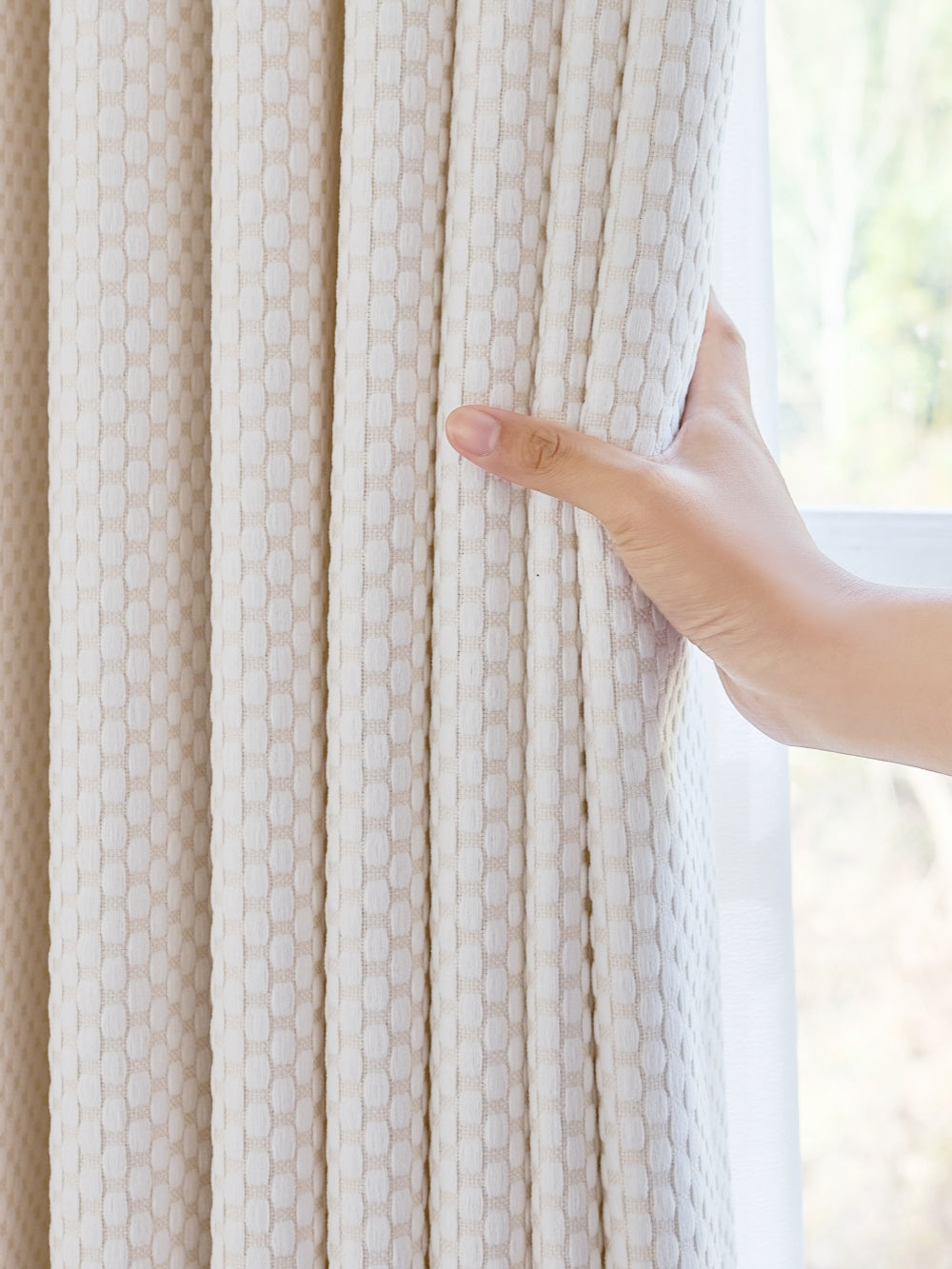 Heavyweight blackout noise cancelling curtains in pearl-inspired design, hand shown adjusting textured fabric.