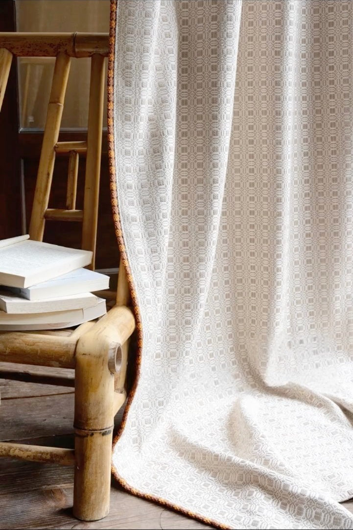 Elegant vintage curtains with subtle geometric pattern and brown trim, draped beside rustic wooden chair with books, creating cinematic vintage ambiance
