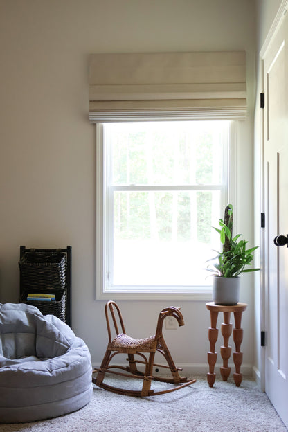 A cozy room featuring a rocking chair by the window, with eco-friendly Roman blinds for enhanced safety and child-friendly settings.