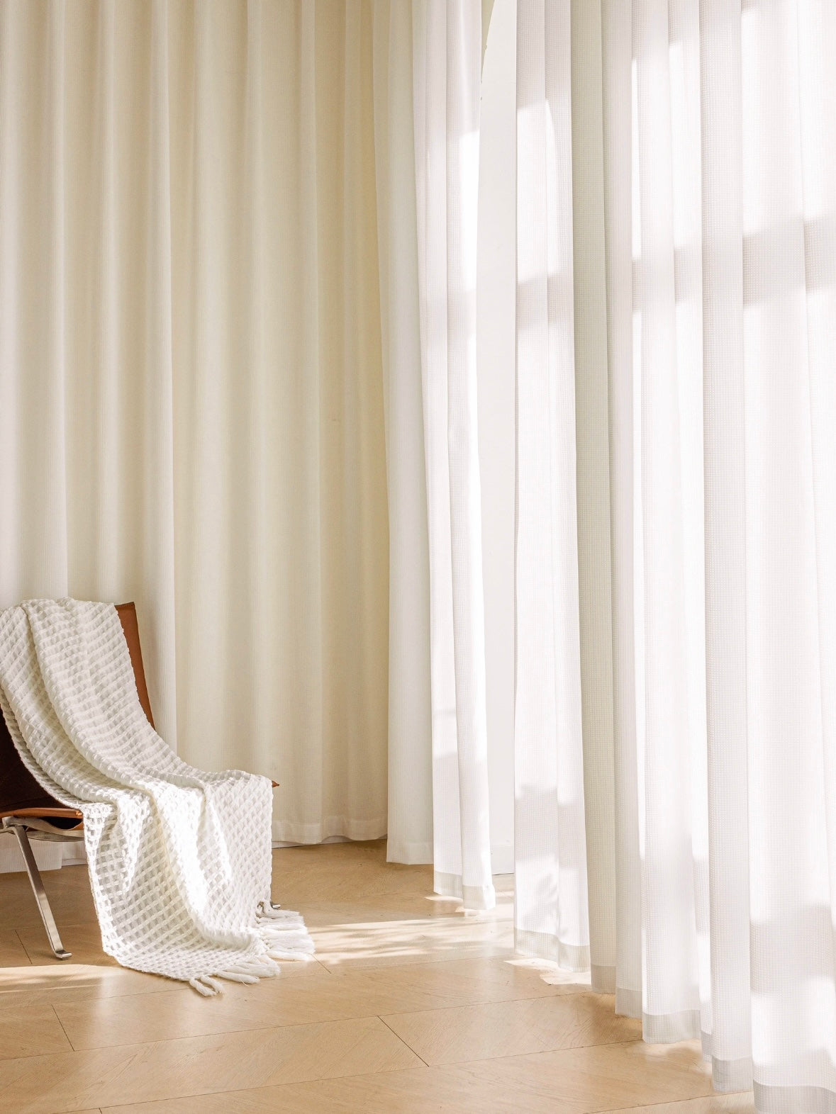 Cozy interior setup with floor-to-ceiling sheer white curtains by EaseEaseCurtains, wooden chair and white blanket in sunlight, symbolizing tranquility and ethereal home decor