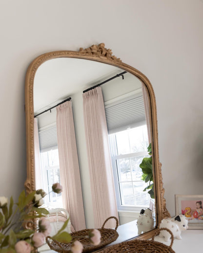 Elegant interior with blush pleated drapes reflected in an ornate gold mirror, enhancing a serene home decor ambiance
