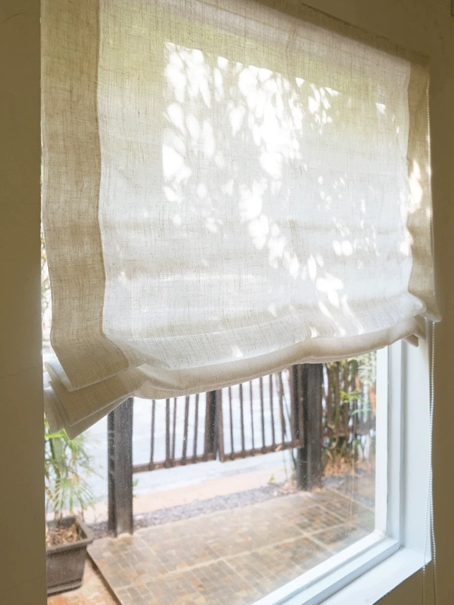 Light filtering relaxed Roman shades with gracefully curved bottom in premium linen gauze, allowing gentle sunlight for a French-style interior elegance.