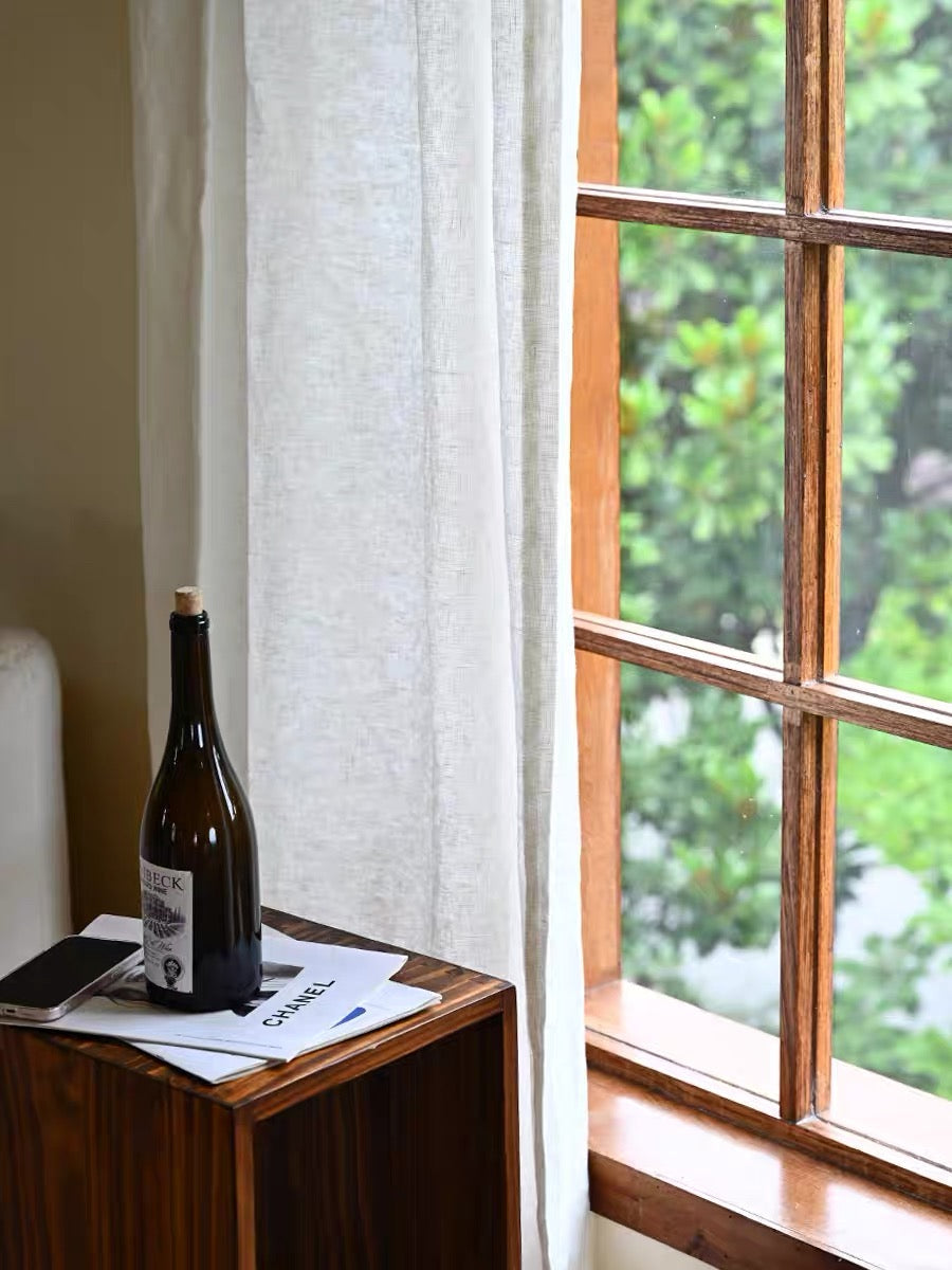 white sheer linen curtain hanging by wooden window with outdoor greenery visible