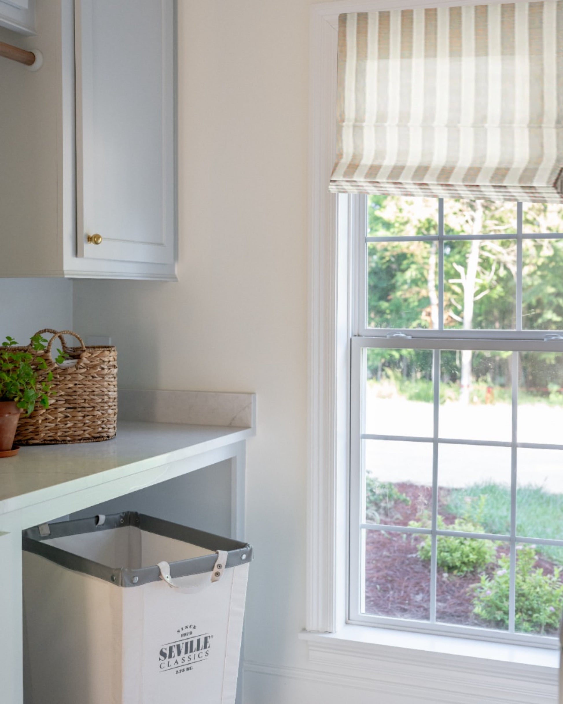 Striped Roman Shades with cordless lift in a bright kitchen window showcasing light filtering custom fabric