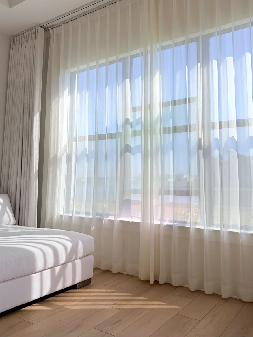 Cream sheer curtains with radiant shimmer filtering sunlight in a bright sunroom