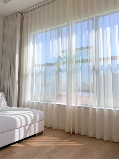 Cream sheer curtains with radiant shimmer filtering sunlight in a bright sunroom