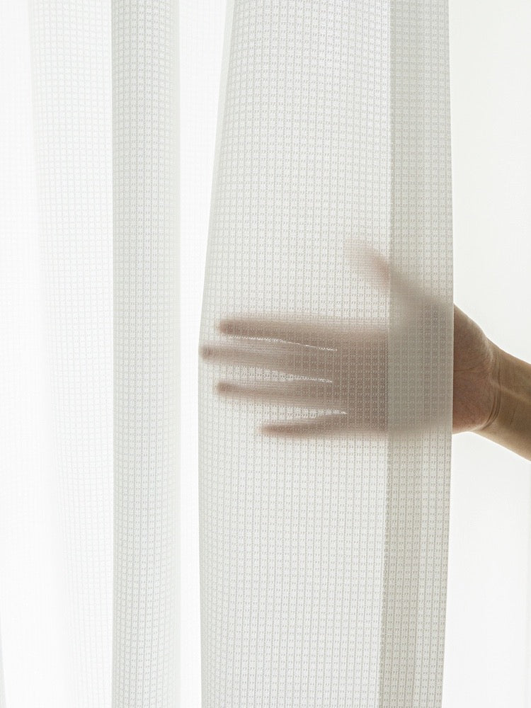 Hand demonstrating the sheerness of the premium white sun-blocking sheer curtain with waffle pattern texture
