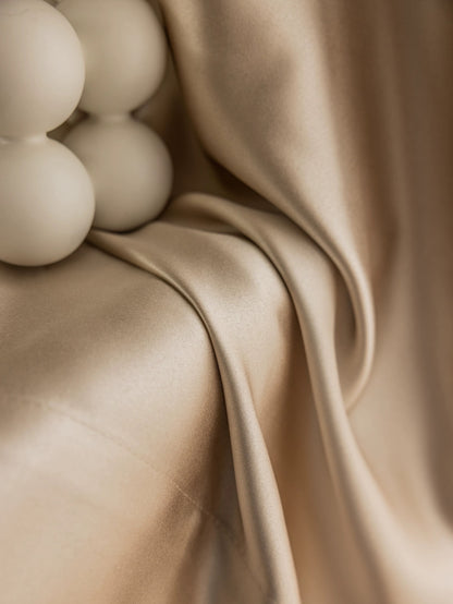 Luxurious silk-like drape in creamy beige featuring a smooth, glossy texture and elegant folds, accented by spherical curtain accessories