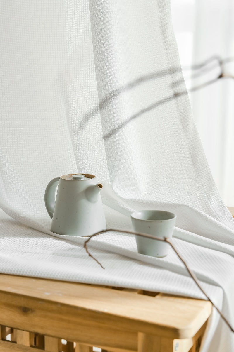 Wooden table with teapot and cup on it, set against EaseEase Premium White Sun-Blocking Sheer Curtain with UV Protection and Waffle Pattern.