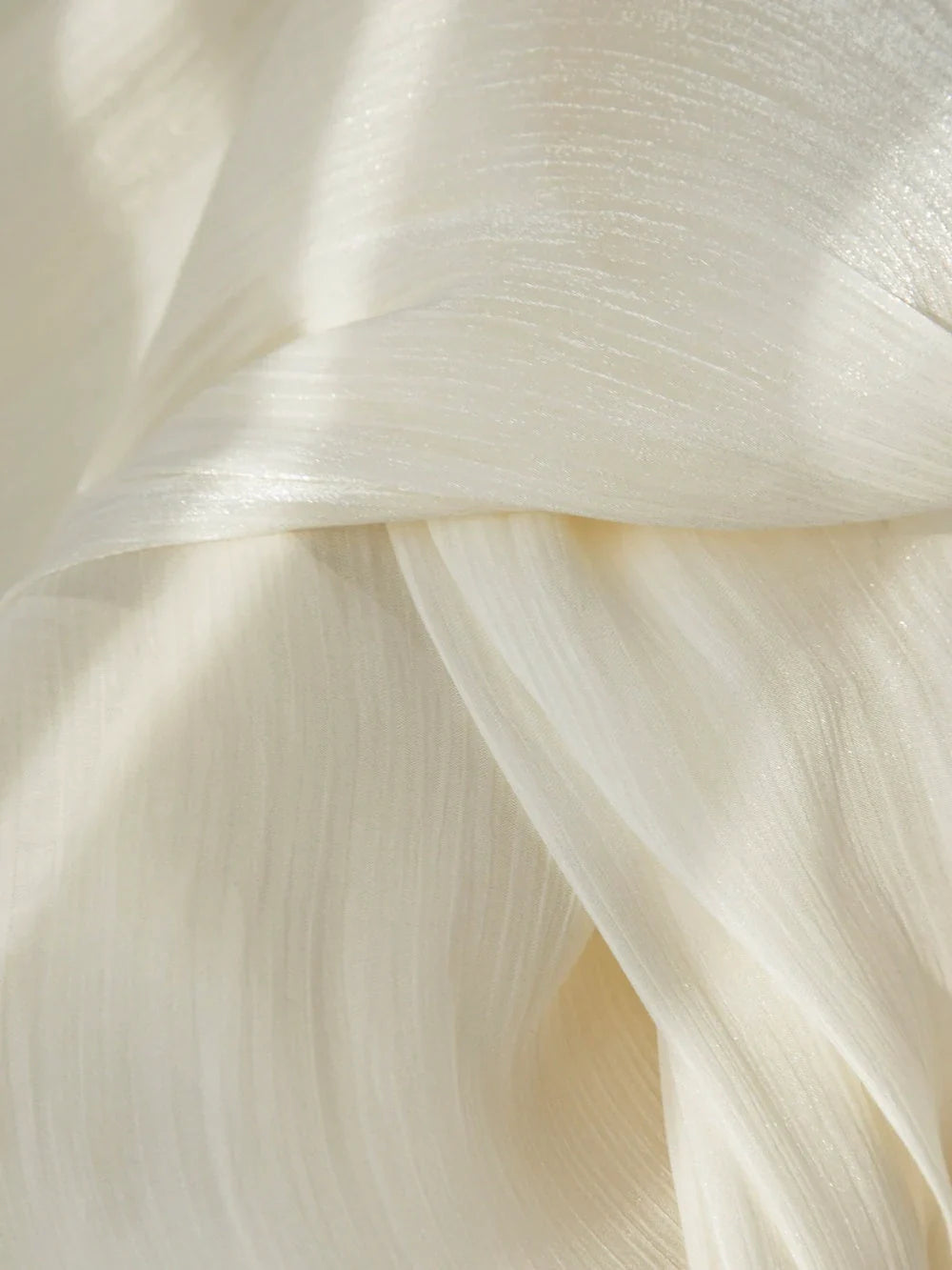 Close-up of cream-colored sheer curtains with a radiant, pearlescent shimmer and soft flowing texture.