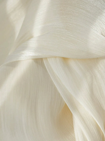 Close-up of cream-colored sheer curtains with a radiant, pearlescent shimmer and soft flowing texture.