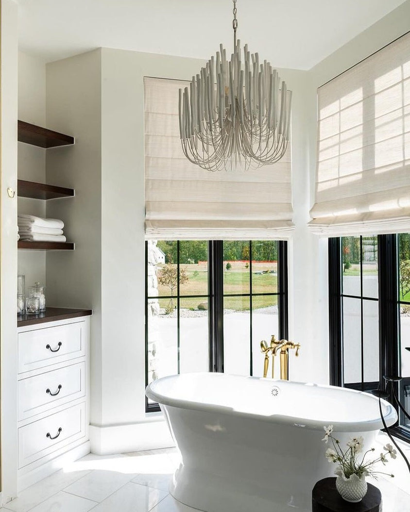 Custom Roman shades in a modern bathroom with a freestanding tub and chandelier.