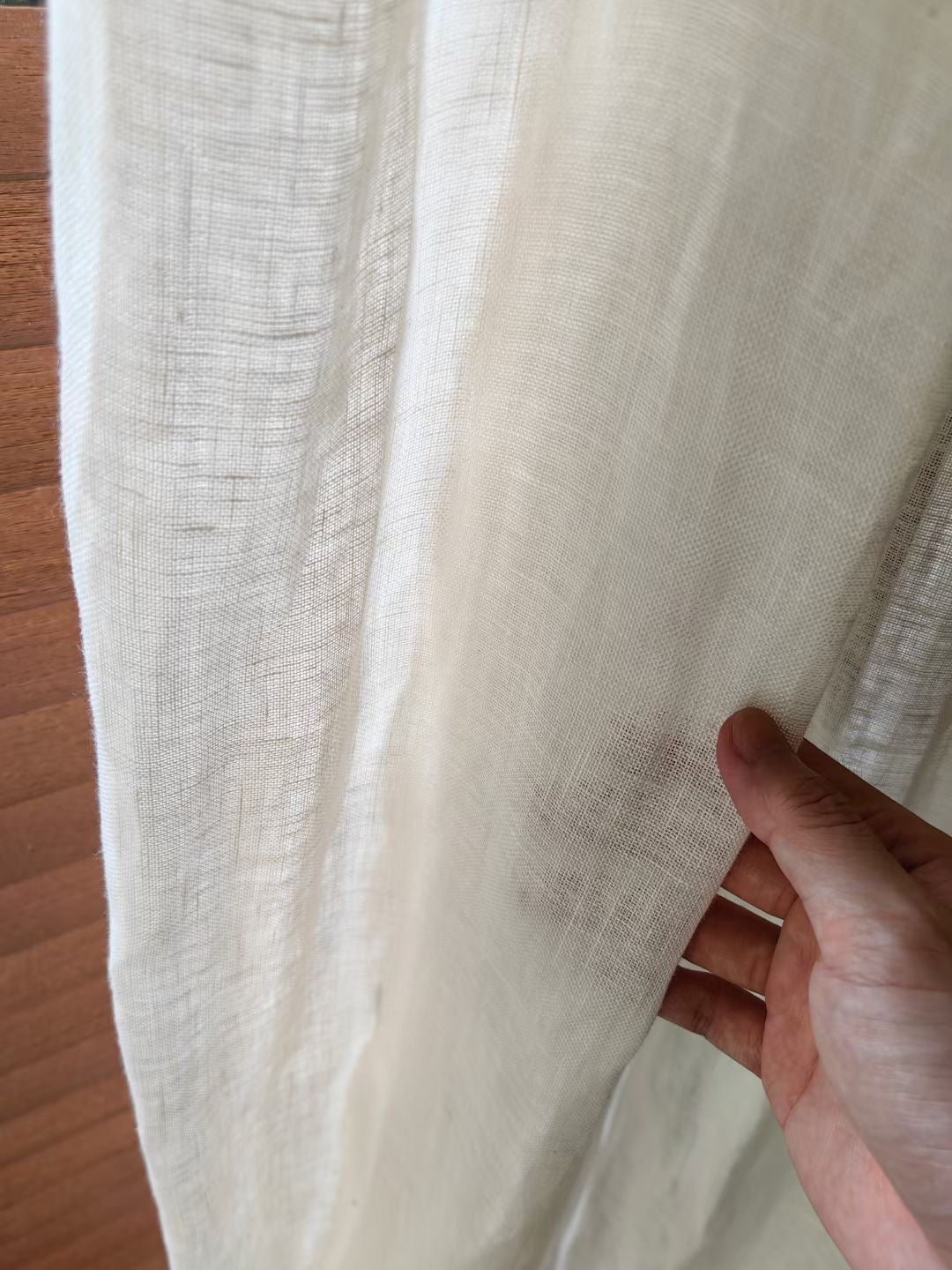 Close-up of hand holding French-imported white linen curtain, showcasing the natural weave and luxurious texture, ideal for sophisticated home decor