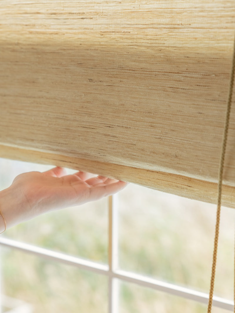 Mildew-resistant natural ramie bamboo shades in cashew with soft woven texture, filtering light softly through a window.