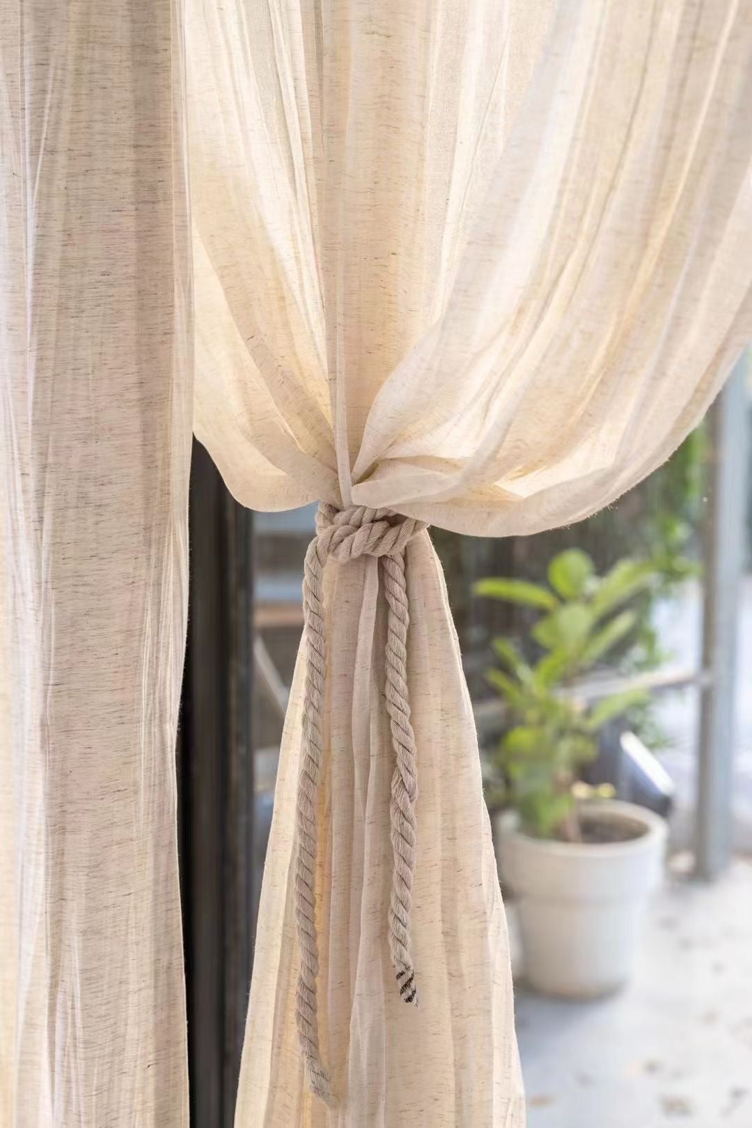 Lightweight crinkled linen gauze drapes tied back, light-filtering for a breezy, airy look.