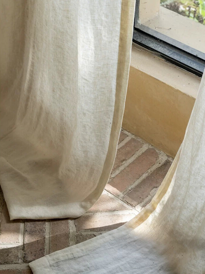 Ivory white linen curtains made from 100% pure French flax, softly draping in natural light by a window.