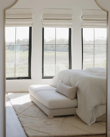 Minimalist bedroom with cordless custom roman shades on three windows, soft neutral tones, and cozy seating area.