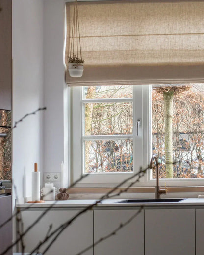 Cordless custom roman shade in natural linen fabric softly draping over bay window with light-filtering and blackout options