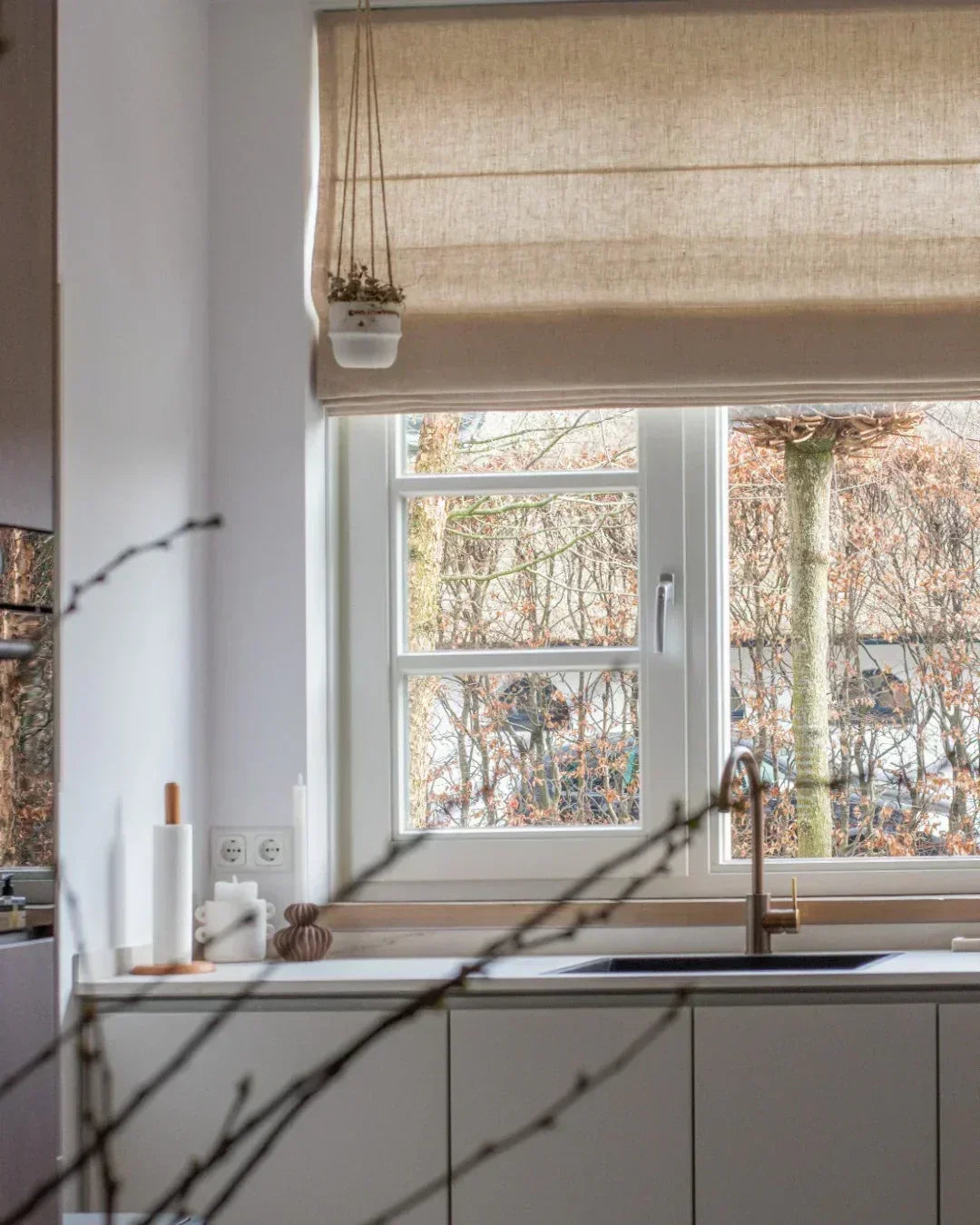 Cordless custom roman shade in natural linen fabric softly draping over bay window with light-filtering and blackout options