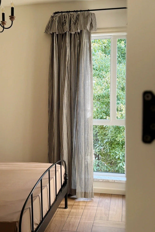 Classic linen striped curtains with fine vertical stripes hanging by a window in a cozy bedroom.