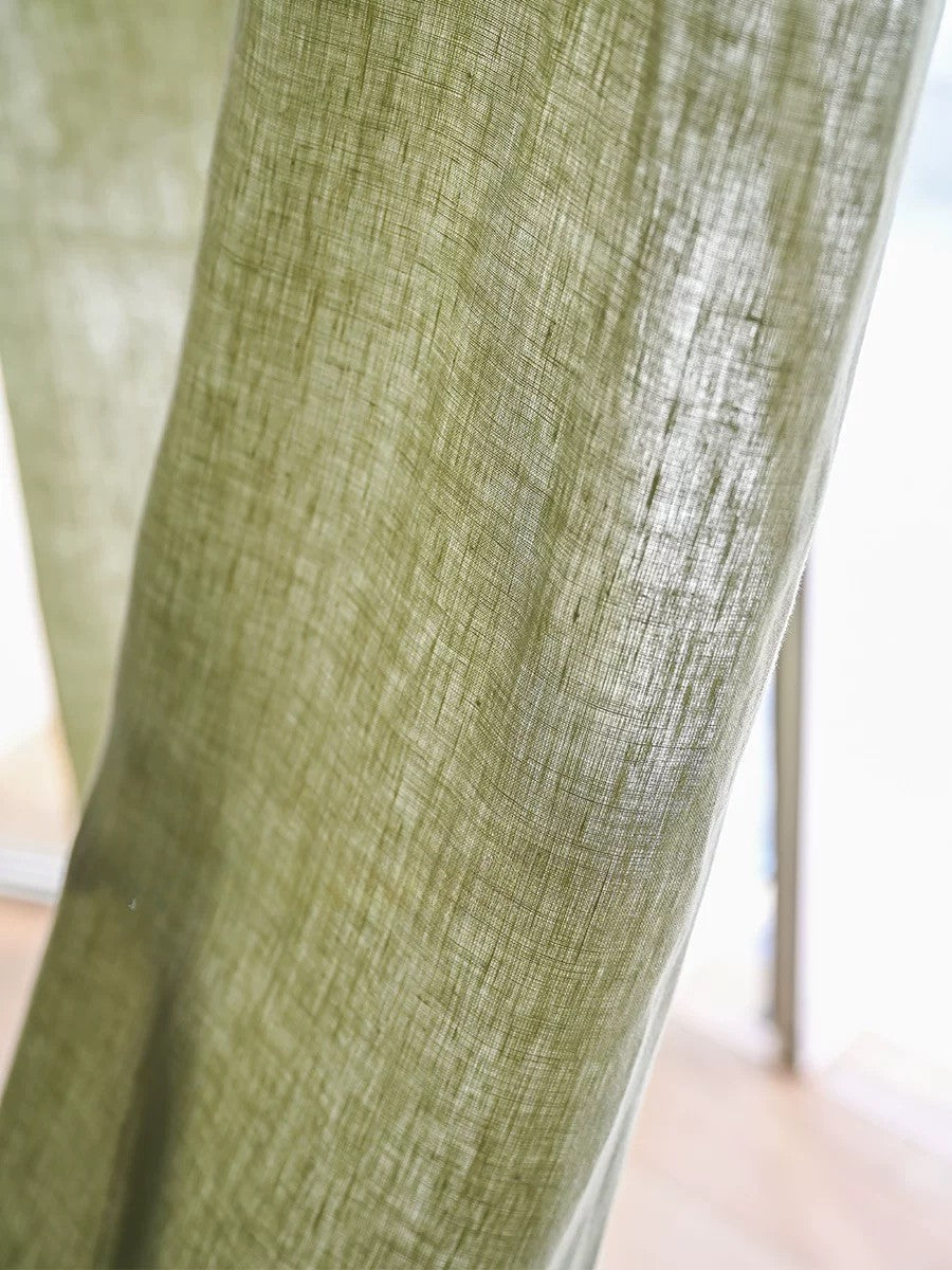 Close-up of eco-friendly sage green curtains made from 100% pure French linen with a natural textured weave and soft, muted green color.