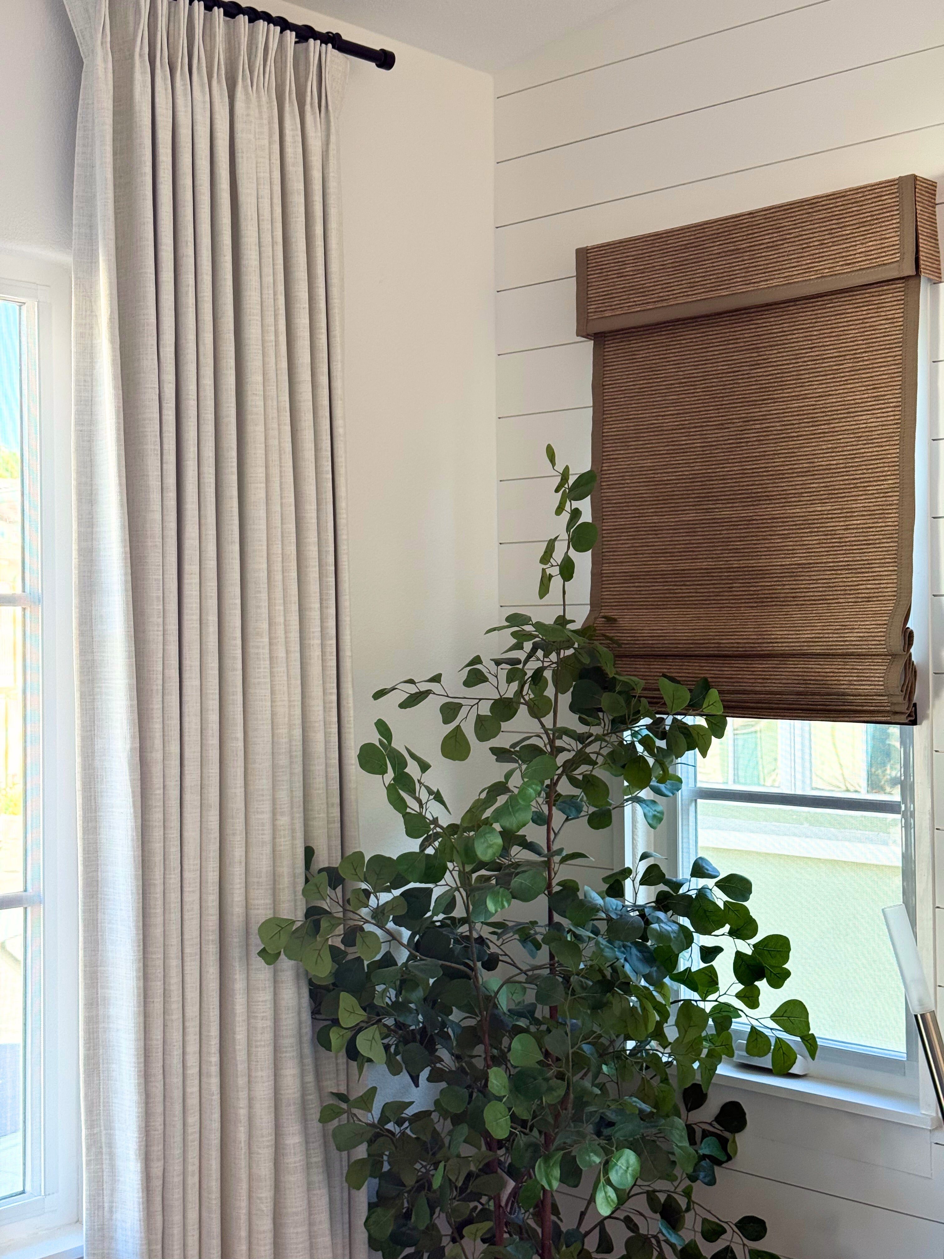 linen blackout curtains in light beige next to a green indoor plant by window with brown roman shade in modern room