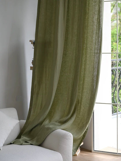 Sage green linen curtains hanging beside a window over a white sofa in a living room
