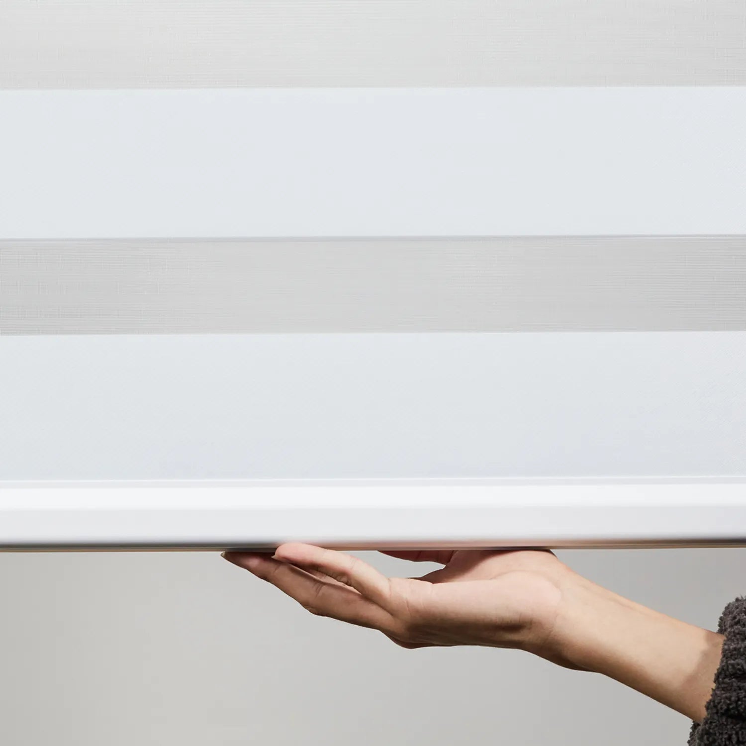 Person adjusting premium Zebra roller shade with dual-layer polyester fabric in light gray and white, showcasing cordless lift functionality