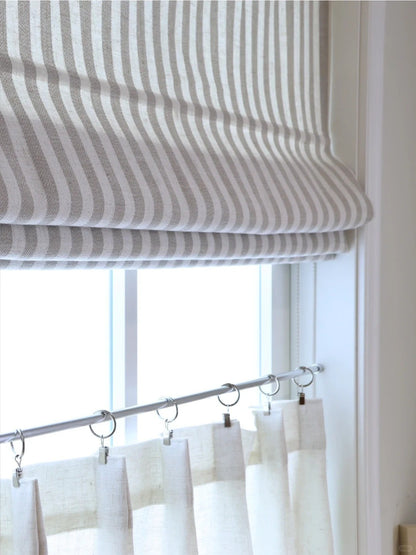Close-up of classic striped roman shades with light filtering fabric over window with sheer curtains below