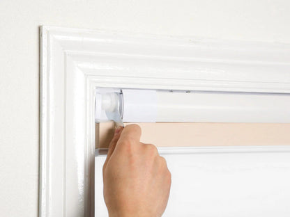 Hand installing no-drill honeycomb shades with silicone no-nail system on a white window frame