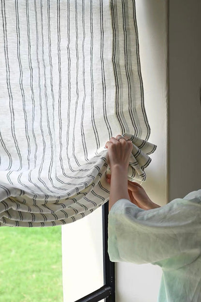 Gray striped roman shades in textured sheer linen, with narrow dark stripes and softly gathered Roman folds.
