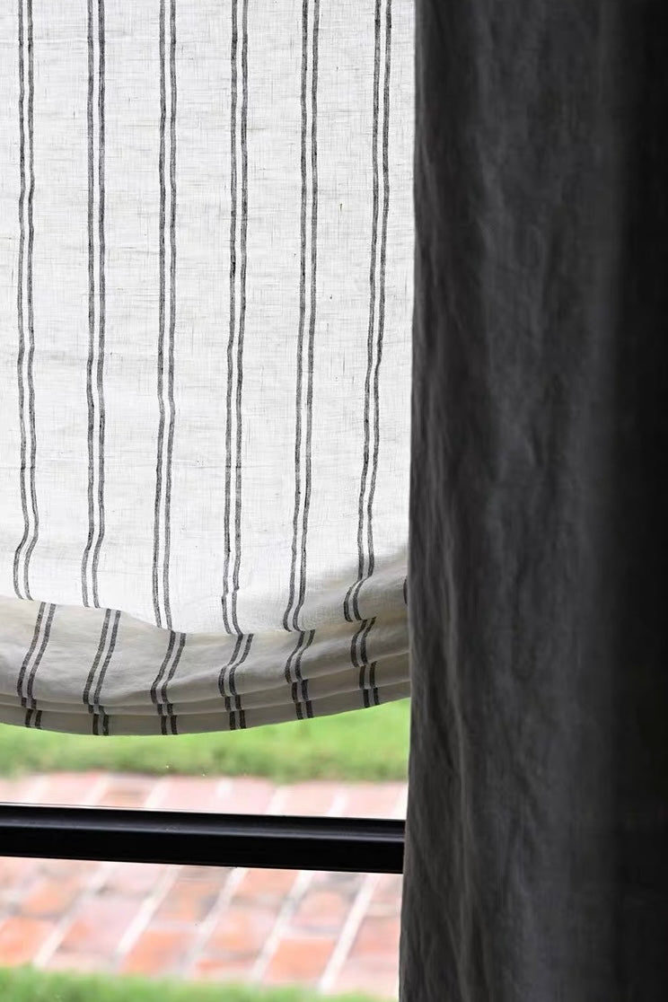 Gray striped roman shades in textured white linen, with narrow charcoal vertical stripes and a softly folded hem.