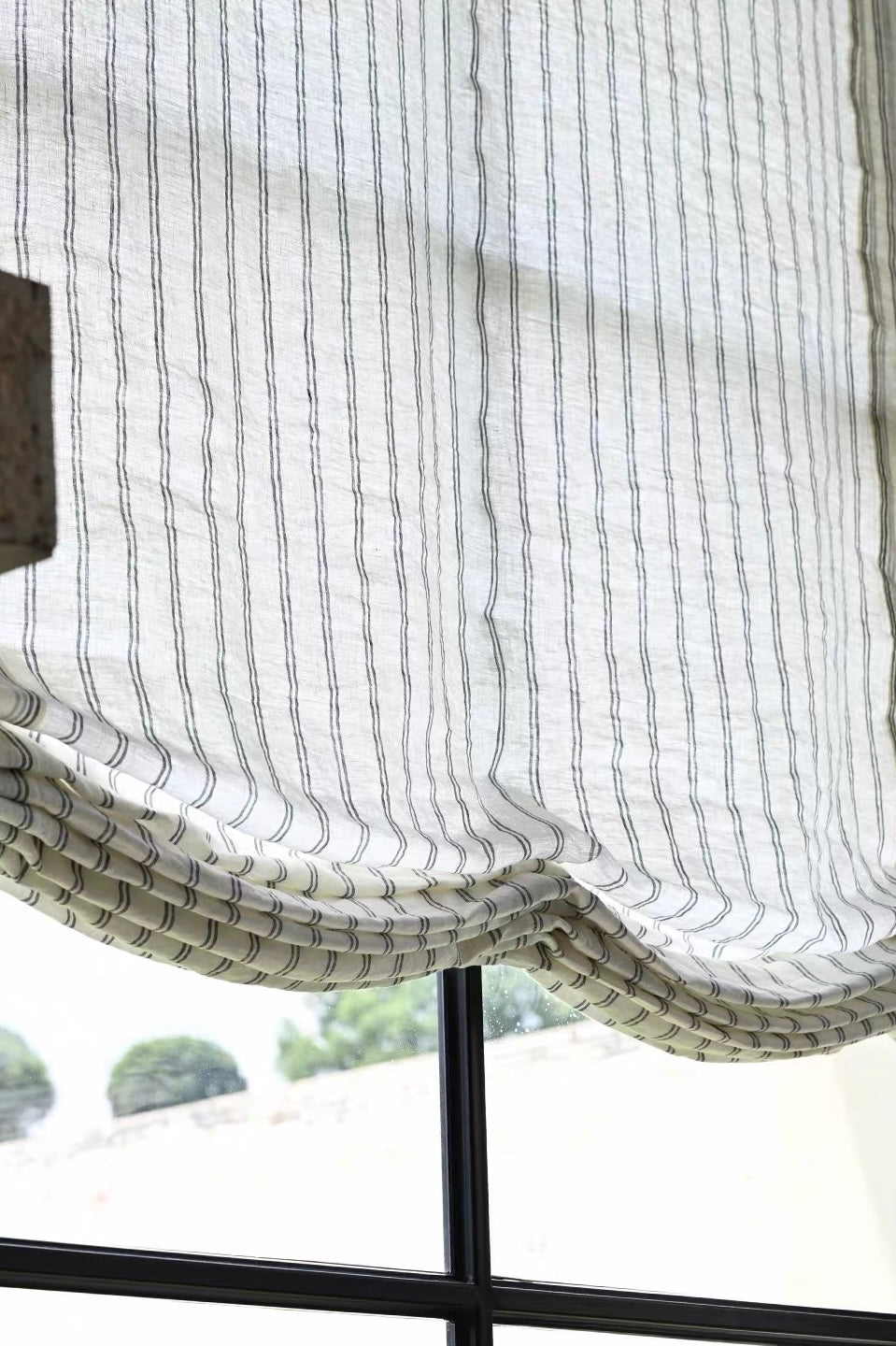 Gray striped roman shades in sheer white fabric with fine vertical gray lines and soft, gathered Roman folds