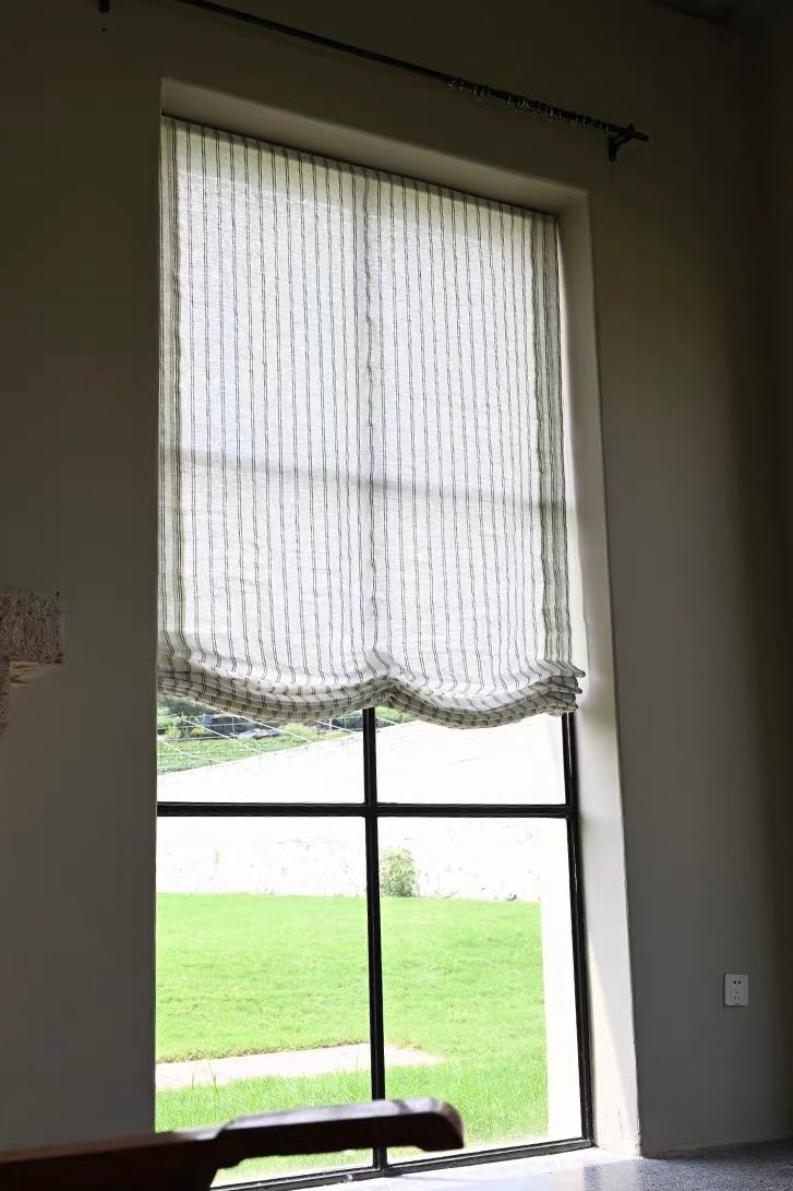 Gray striped roman shades in sheer textured fabric, softly gathered into a scalloped Roman fold at the bottom.