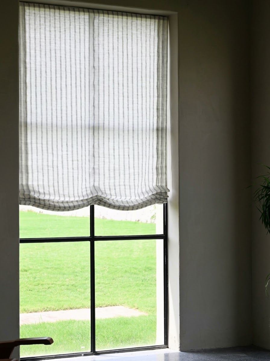 Gray striped roman shades in sheer white fabric with fine vertical gray stripes and softly scalloped Roman folds