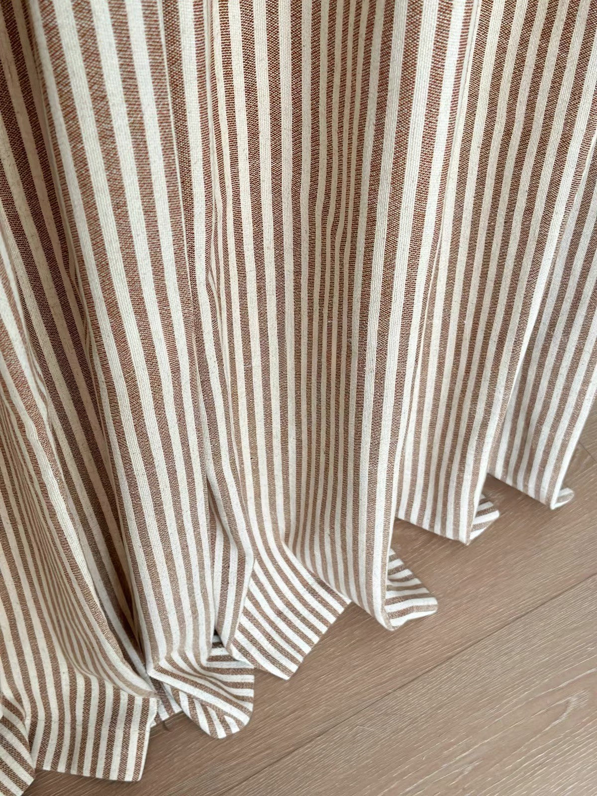 Close-up of brown and cream striped linen curtain hem pooling on a wood floor