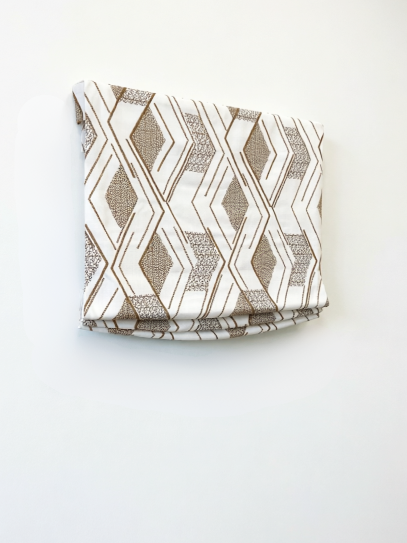 Patterned Roman Shades in cream linen with taupe geometric embroidery, featuring crisp flat folds and raised texture