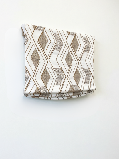 Patterned Roman Shades in cream linen with taupe geometric embroidery, featuring crisp flat folds and raised texture