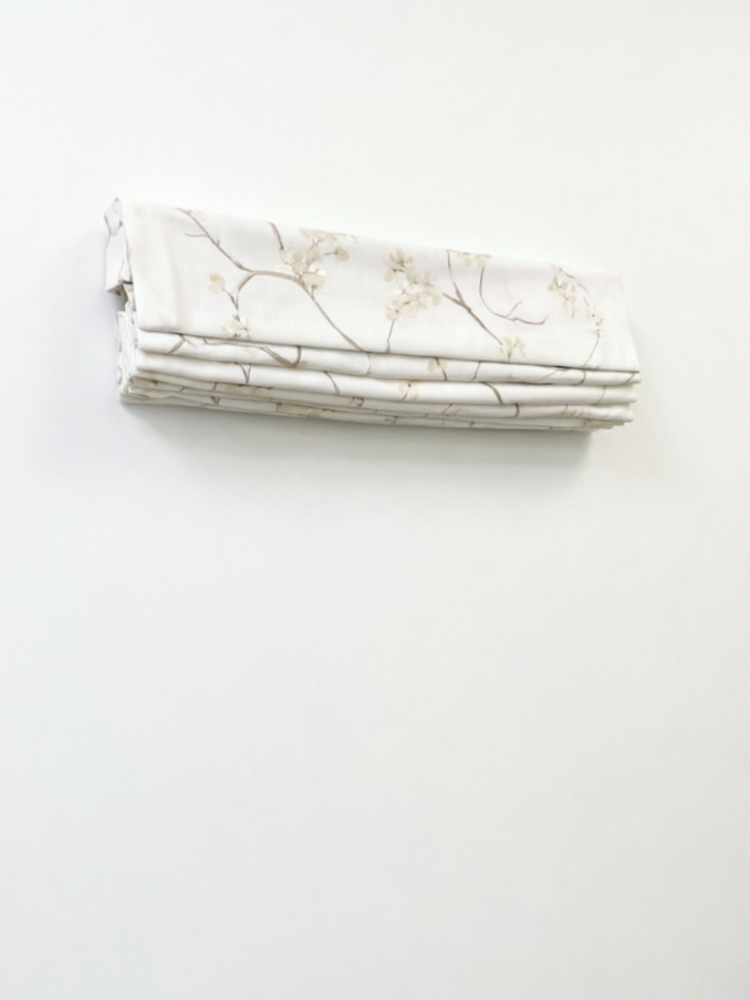 Patterned Roman Shades in ivory linen with delicate embroidered branches and flowers, shown in neat flat folds