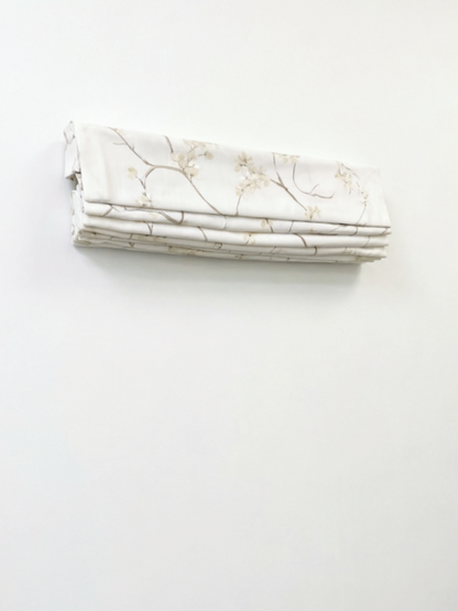 Patterned Roman Shades in ivory linen with delicate embroidered branches and flowers, shown in neat flat folds