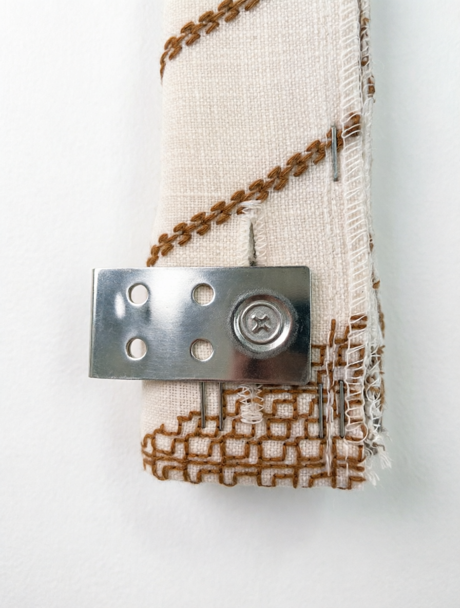 Patterned Roman Shades in natural linen with raised brown French embroidery and a concealed metal mounting bracket visible at the edge