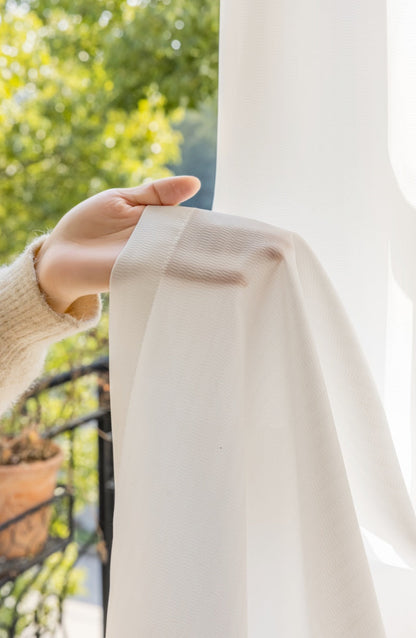 White sheer curtain hanging in a bright room, providing privacy and natural light.
