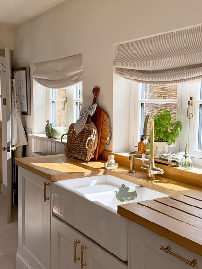 Relaxed Roman shades in striped beige linen with a soft curved hem, shown over two kitchen windows
