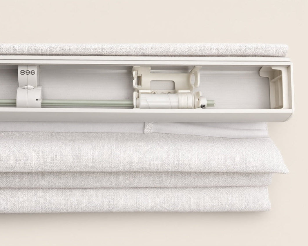 Close-up of a white textured fabric blind or roller shade with a white metal roller mechanism and track, shown against a light beige background.