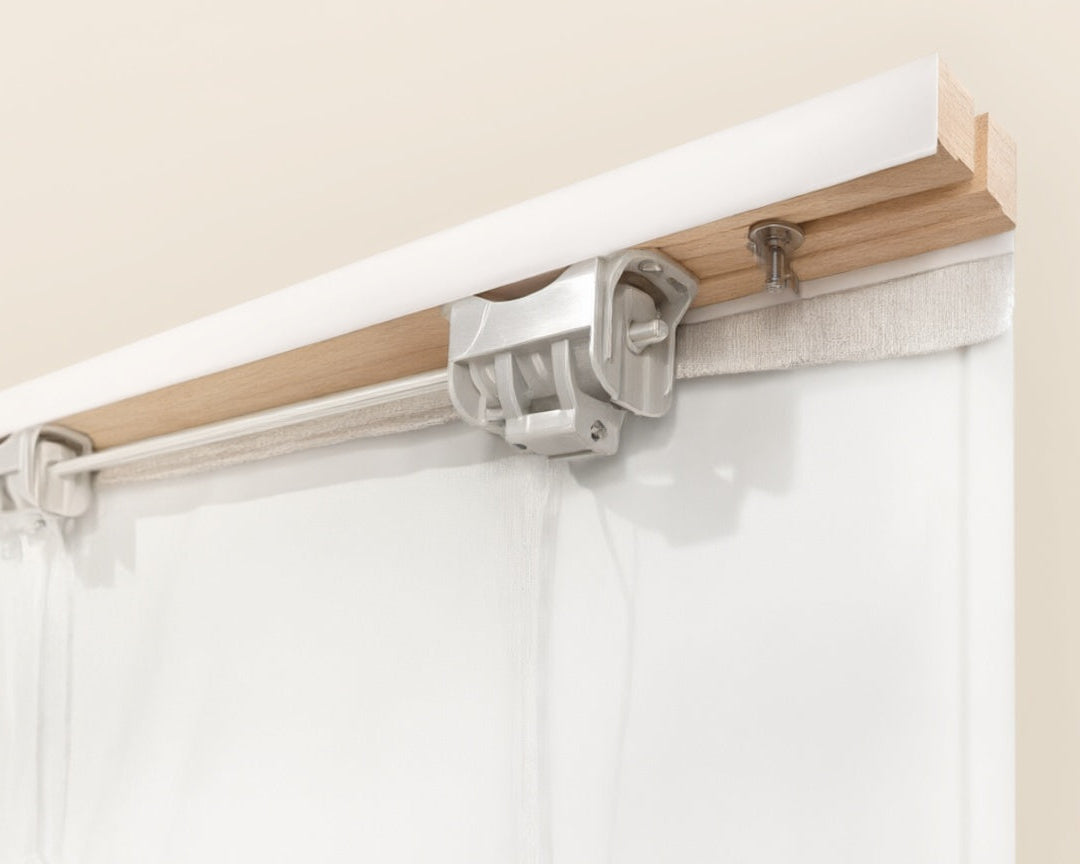 Close-up of a roman shades cordless system with a light wood rail, white roller bar, and silver metal clips holding up white curtains against a beige wall.